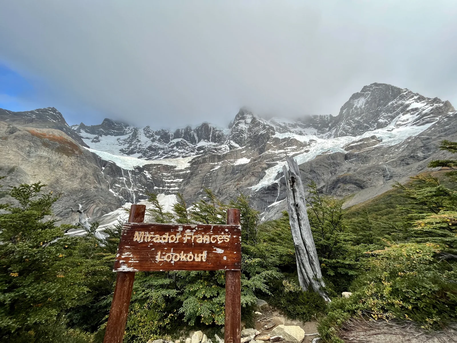 Trail sign and waterfall beneath snow-covered peaks