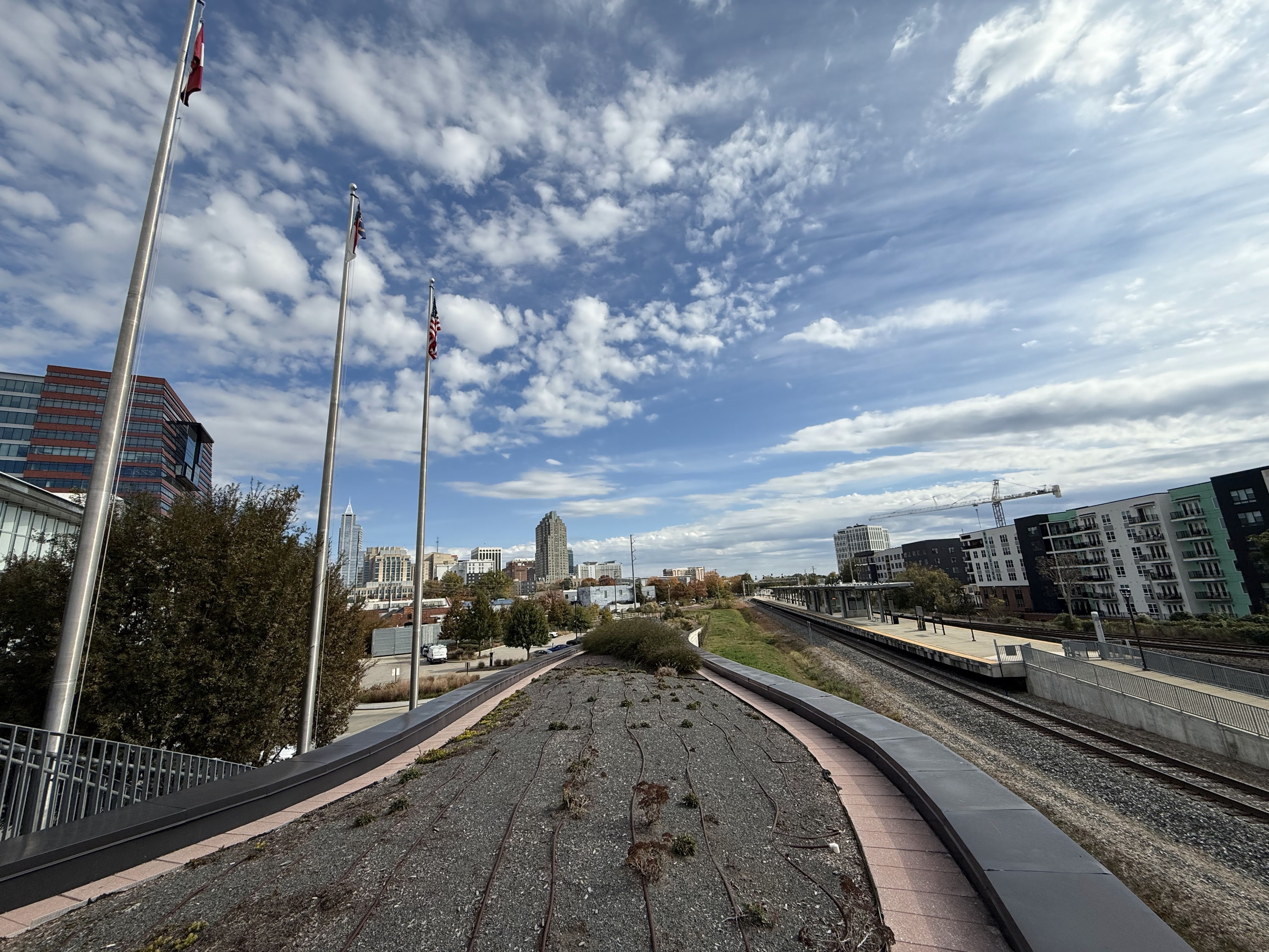 Downtown Raleigh skyline and the platform at Raleigh Union Station beneath a wide, cloud-streaked sky.