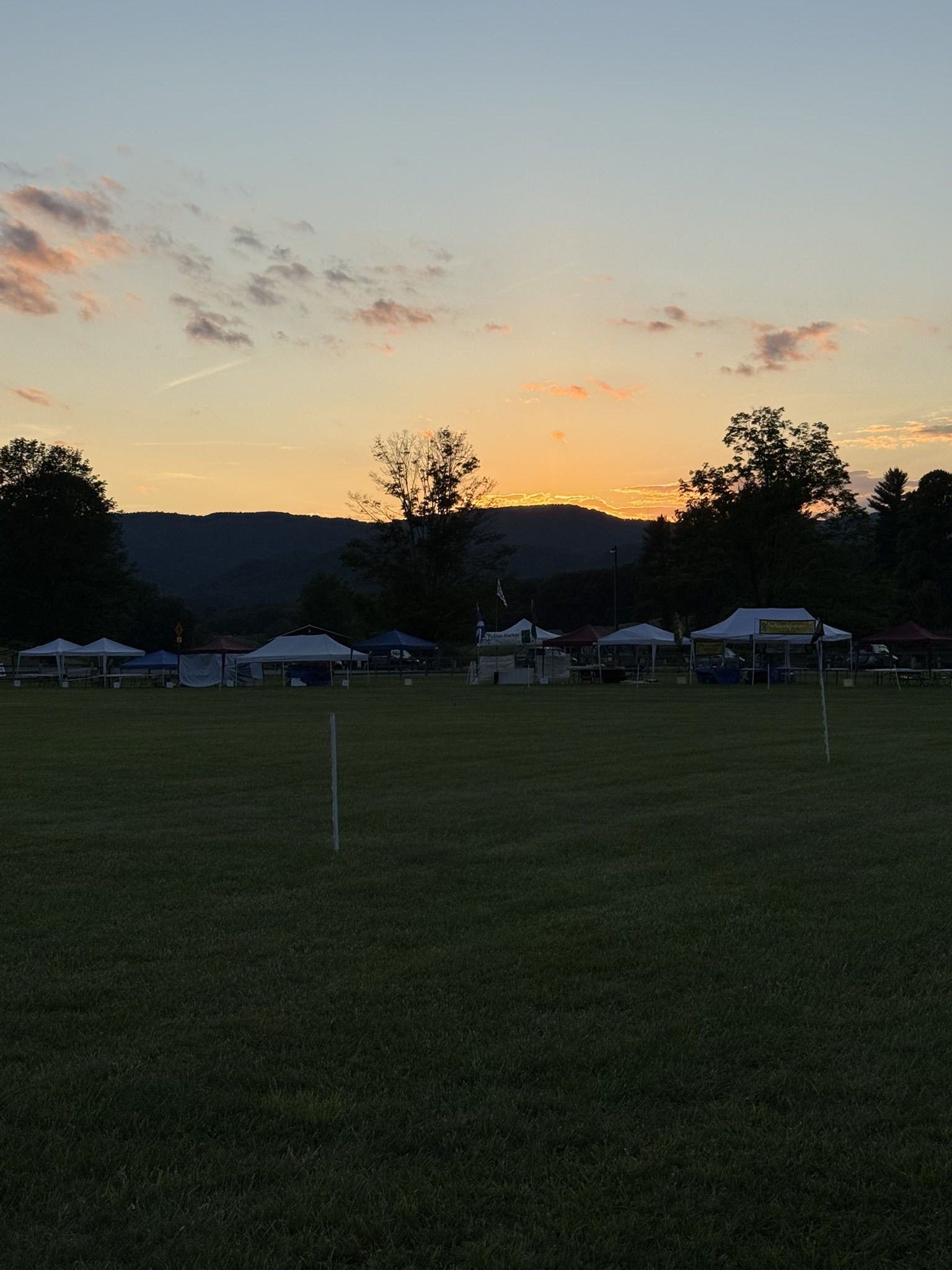 Festival tents spread across a field beneath West Virginia hills at sunset.