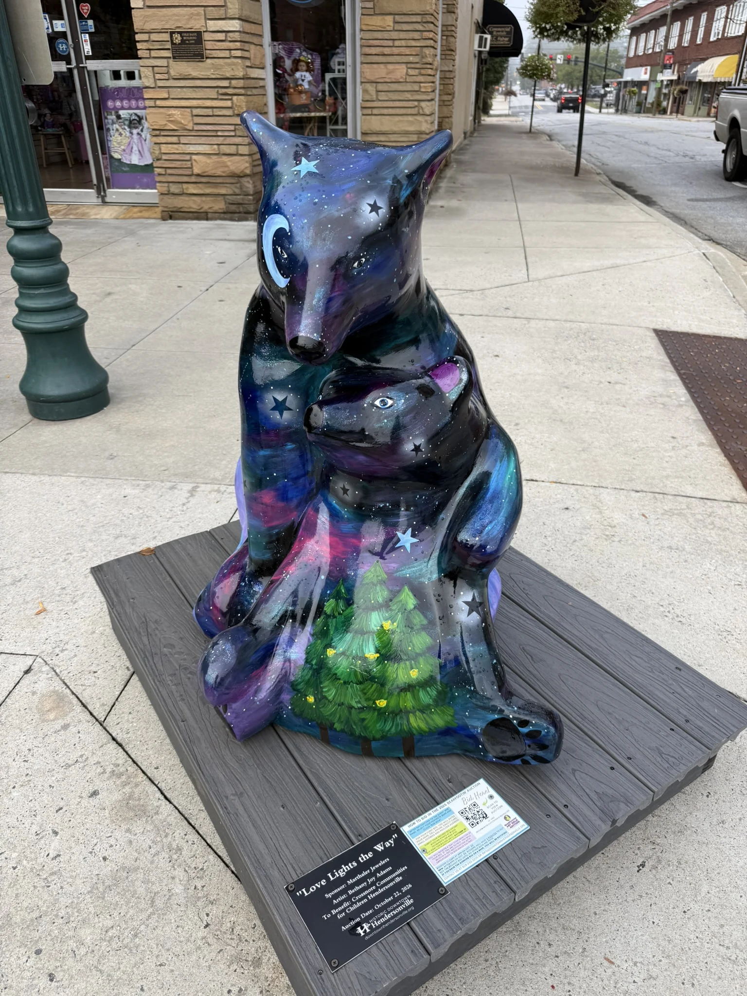 A purple and blue bear statue painted with stars on a downtown Hendersonville sidewalk.
