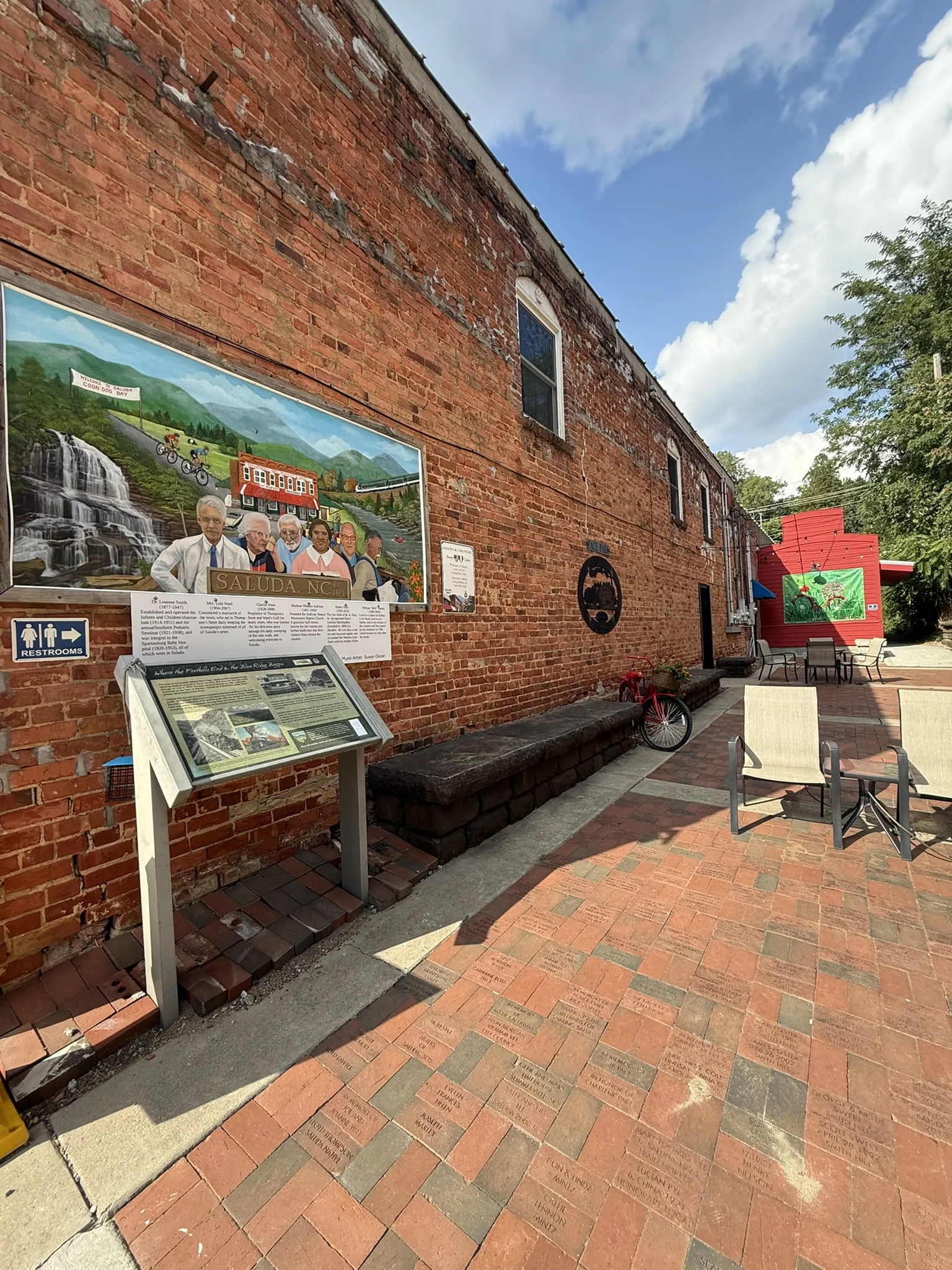 A brick passage in Saluda with a painted mural, benches and shop displays.