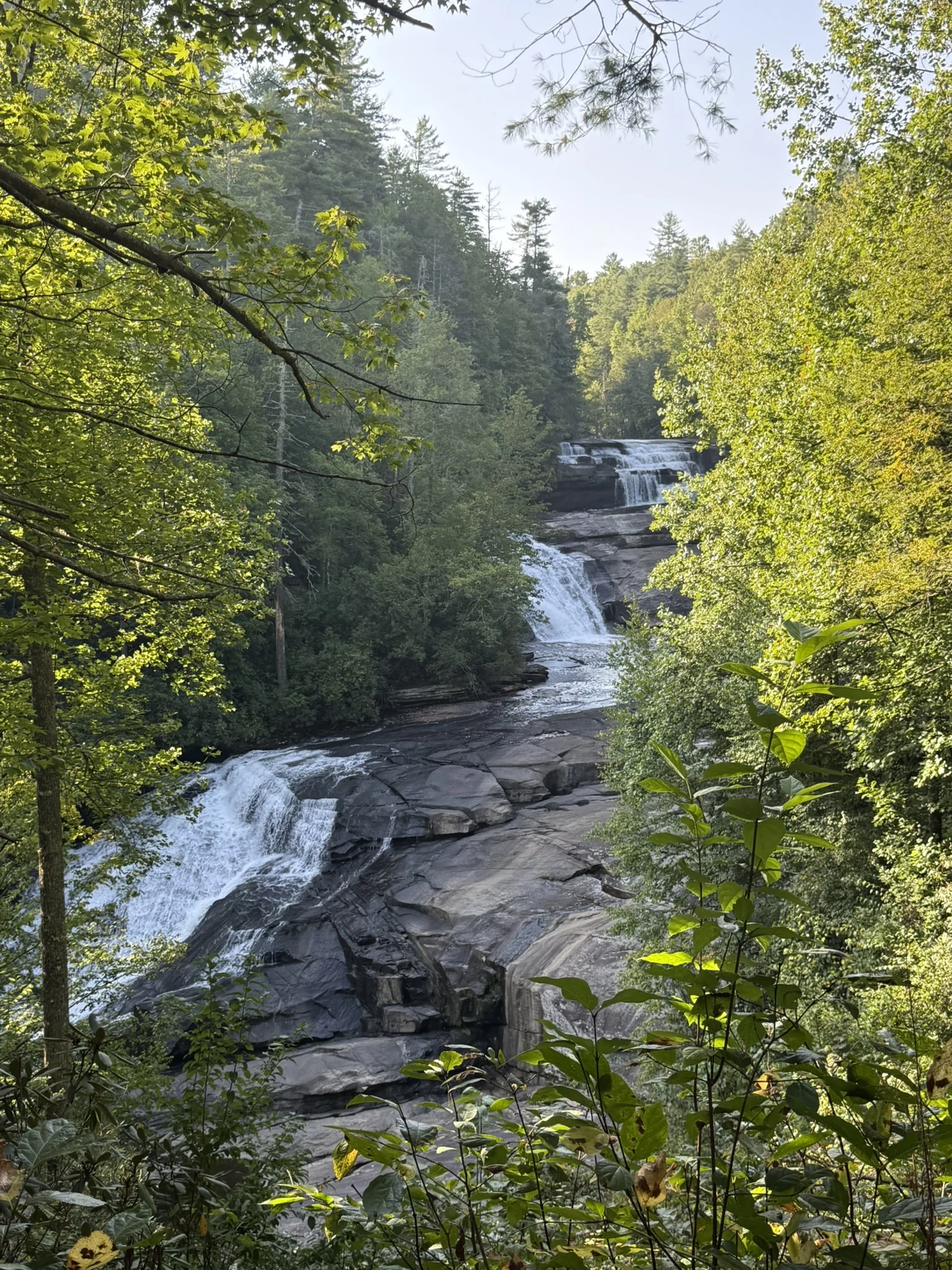 The successive cascades of Triple Falls framed by sunlit green trees.