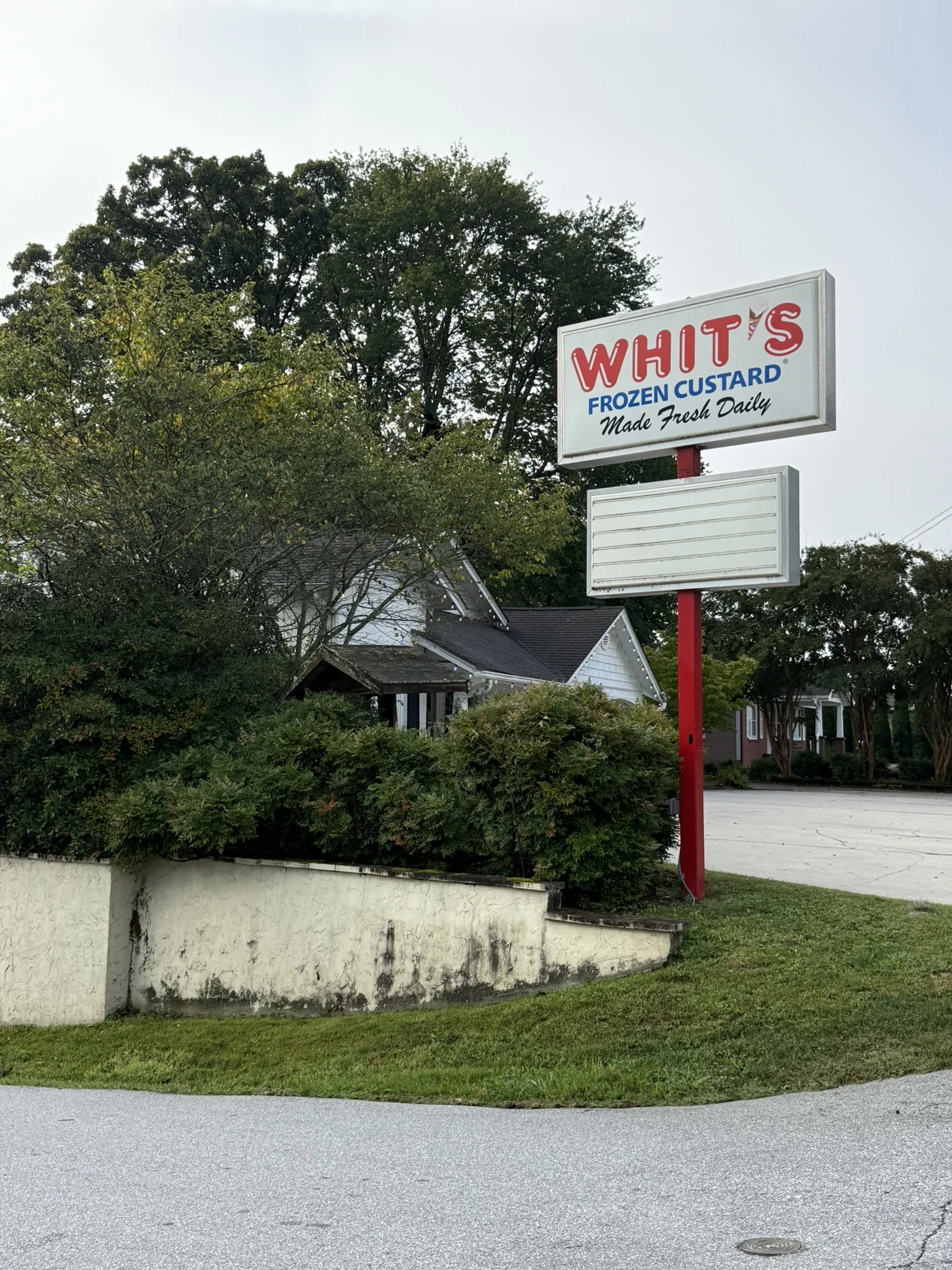 A roadside Whit’s Frozen Custard sign beside trees and the Hendersonville shop.