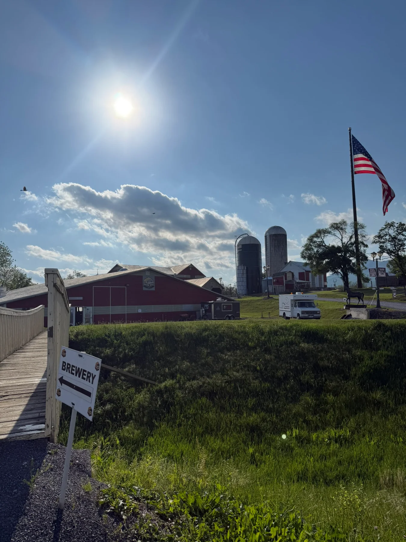 Cave Hill Brewery on a sunny farm property with red barns, silos, and an American flag.