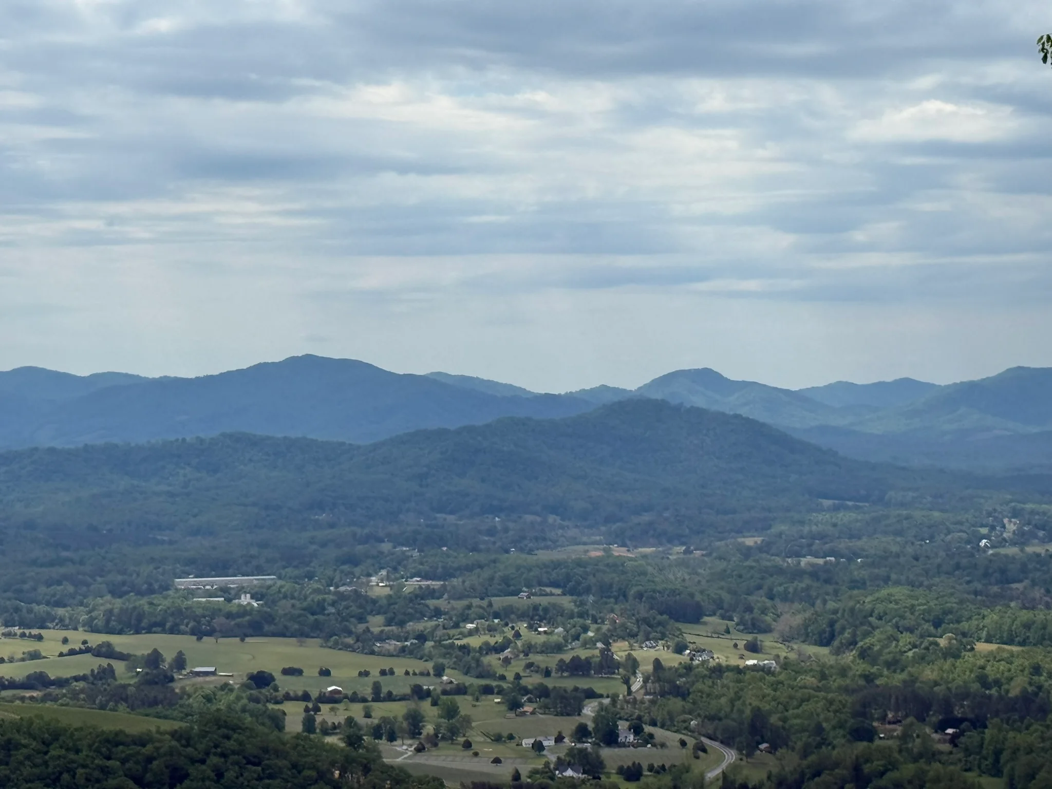 A Massanutten overlook view across a green valley and distant Blue Ridge mountains.