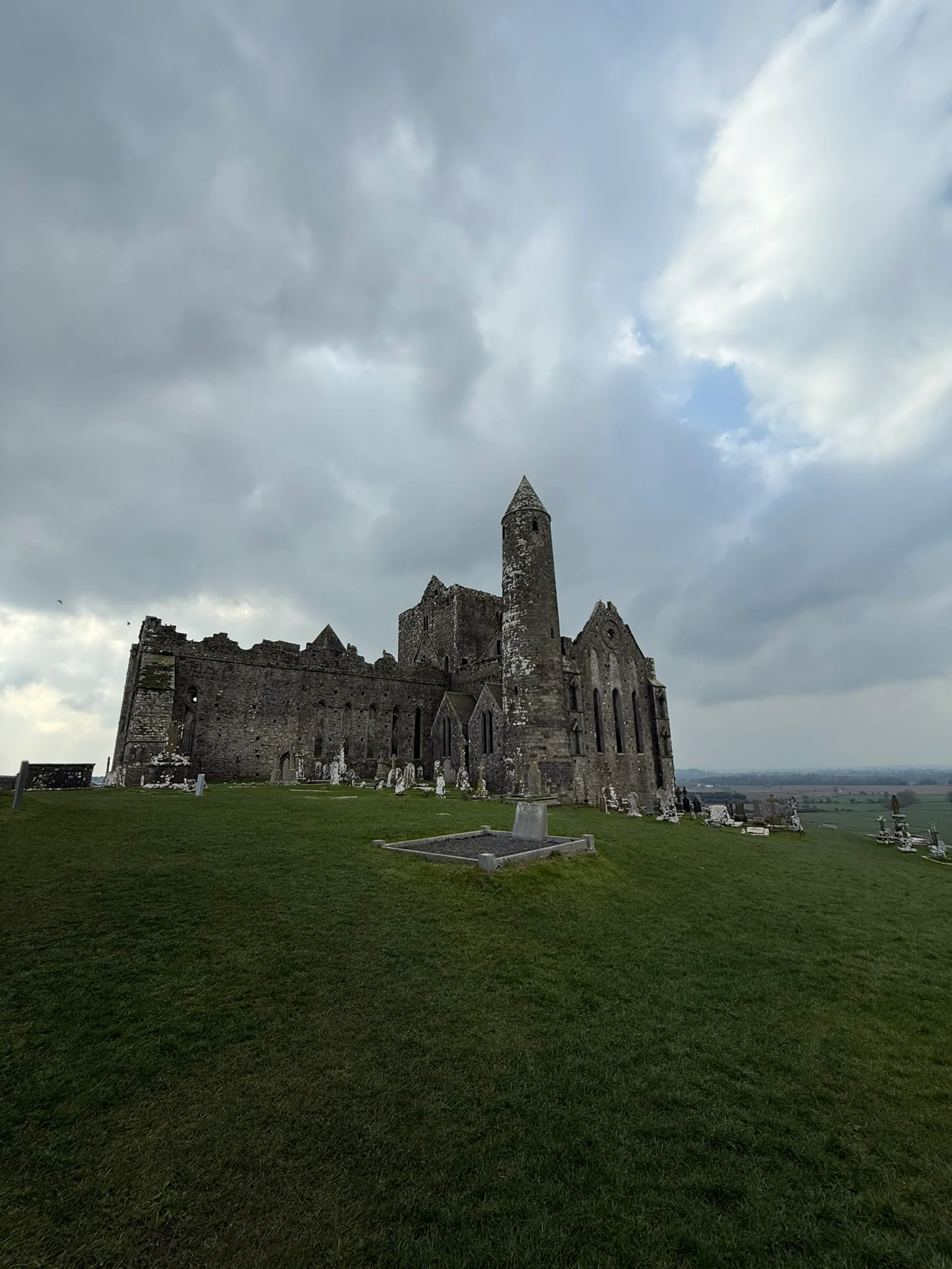 The Rock of Cashel standing on a green hill beneath dramatic gray clouds.